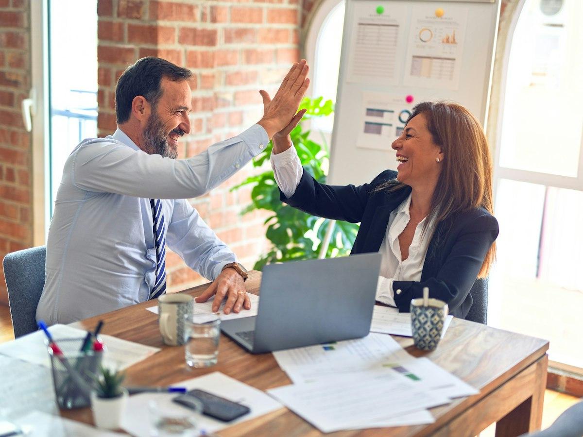 Two colleagues sharing a high five over a laptop